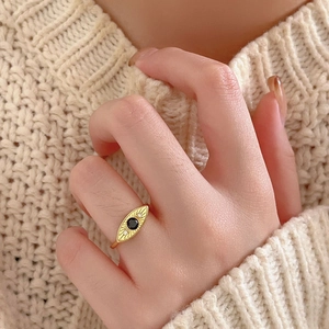 Detail shot of gold evil eye ring with black stone and diamonds on a beige sweater