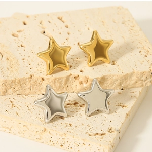 Close-up of minimalist gold and silver star earrings on a beige stone pedestal