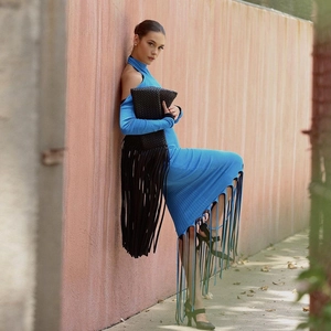 Détail de la robe en tricot bleu avec franges et pochette en cuir tressé noir