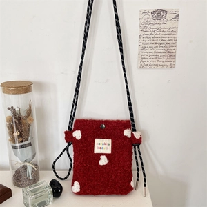 Detail of red fleece phone bag with white hearts and woven strap on white wall background