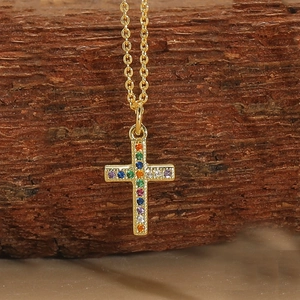 Close-up of golden cross pendant with colorful rainbow zircons on a delicate chain