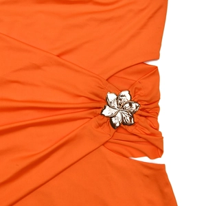 Gros plan sur un tissu plissé orange orné d'une boucle fleurie en métal doré à la taille de la robe