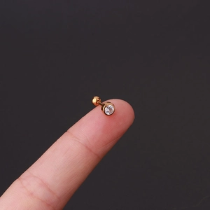 Macro view of a tiny gold stud earring with clear gemstone held on a fingertip for size