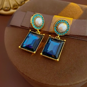 Close-up of vintage gold earrings with deep blue square crystals and white pearls
