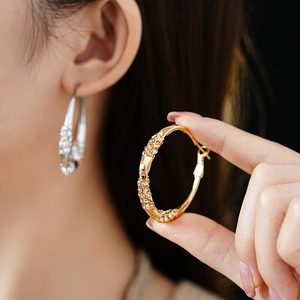 Macro detail of large twisted hoop earrings with pave diamonds in gold and silver finish
