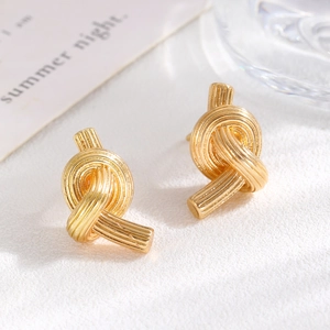 Macro shot of gold knot earrings on a textured background with natural lighting and shadows