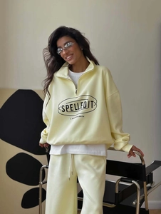Close-up of SPELLEDIT brand logo print on light yellow half-zip knitted sweatshirt