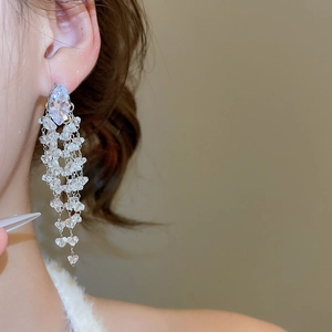 Macro shot of silver needle tassel earrings with clear rhombus crystals on female model