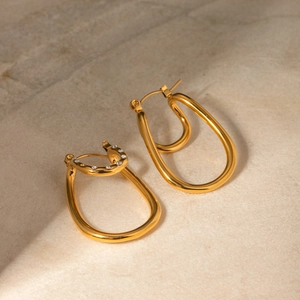 Dettaglio macro degli orecchini curvi in oro 18k con strass bianchi brillanti e design unico