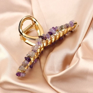 Macro view of gold alloy hair claw clip with amethyst crystal stones on satin fabric