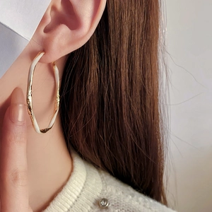 Close-up of a large gold and white enamel oval hoop earring with hammer texture detail
