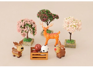 Miniature dollhouse set featuring blooming trees, deer figurines, and a tiny crate with balls