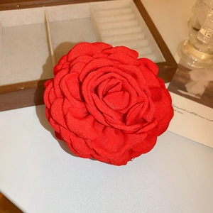 Macro detail of a red fabric flower hair claw with satin texture on a wooden jewelry box