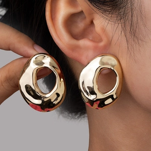 Close-up of oversized irregular gold geometric earrings showing size and polished finish