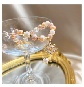 Macro detail of multi-colored pearl bracelet with zircon sunflower pendant on silk background