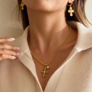 Close-up of gold stainless steel cross necklace and matching hoop earrings on model