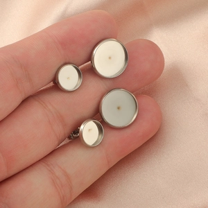 Hand holding silver stainless steel earring stud bases with beige resin inlay on silk