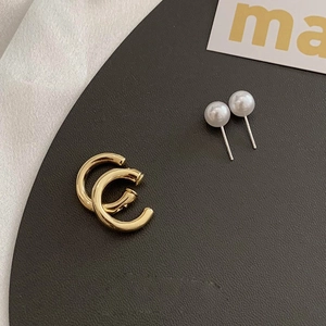 Detail of C-shaped gold metal earrings and white pearl studs on a textured base