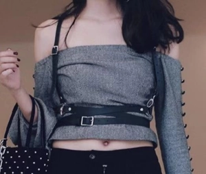 Detail of a black punk leather body harness with metal buckles on a woman's grey outfit