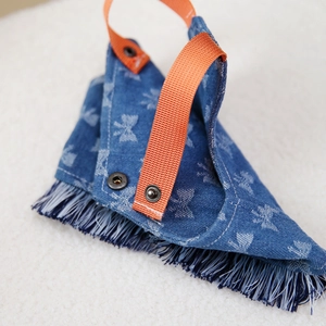 Denim pet bandana with orange nylon strap and blue fringe detail on white plush mat