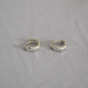 Dettaglio di orecchini a cerchio in argento con trama a bambù su tessuto grigio