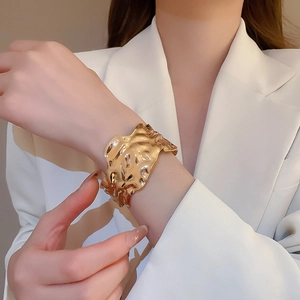 Detail of a golden hammered metal cuff bracelet with irregular wavy edges on a wrist