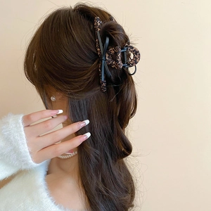 Detail shot of large leopard print hair claw clip worn on curly hair with white sweater