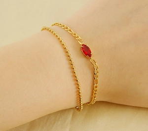 Close-up of double-layer gold beaded and Figaro chain bracelet with red marquise zircon