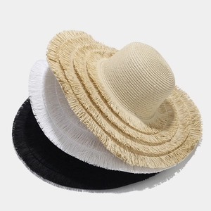 Stack of wide-brim straw hats with fringe edges in cream, white and black for beach sun protection