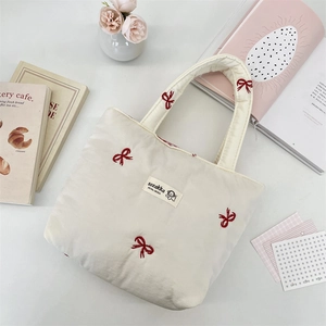 Close-up of quilted cream canvas tote bag featuring delicate red bow embroidery detail