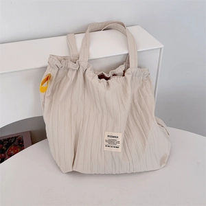 Détail du sac cabas plissé blanc cassé avec accents de ruban jaune et étiquette tissée