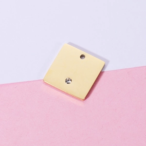 Detailed macro view of a gold square stainless steel charm with a small embedded rhinestone