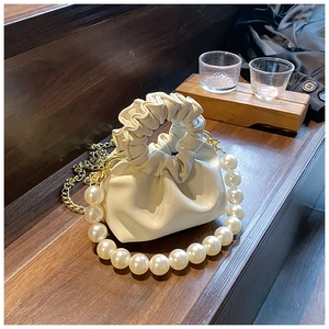 Detail view of white ruched pearl handle handbag with a gold chain on wood surface