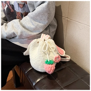 Detail of handmade crochet bucket bag with rabbit ears and strawberry drawstring charms