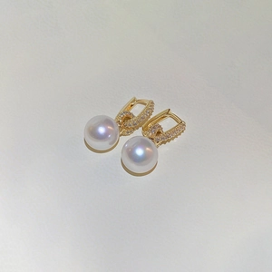 Détail de boucles d'oreilles dorées avec perles blanches lustrées et pavé de zircons chic