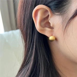 Macro shot of minimalist gold ball stud earring with a matte brushed metal texture