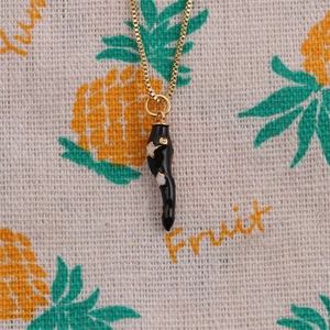Detail of a black chili pendant with white stars on a gold plated necklace chain