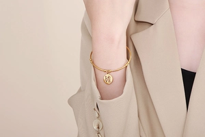Detail of a gold minimalist bracelet with an engraved LOVE and paw print pendant on a model
