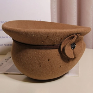 Dettaglio di un basco in lana cammello con elegante fiore e accenti di perle dorate