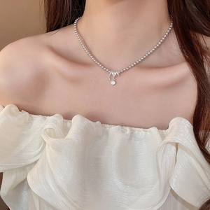 Détail d'un collier à billes argentées avec un pendentif en zircon brillant au cou