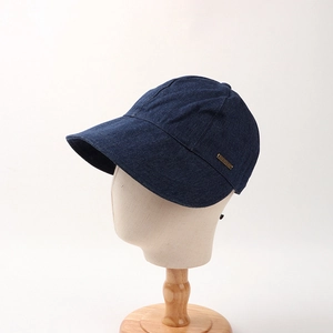 Detailed view of dark blue denim baseball cap with gold JHMY logo plaque on a display head
