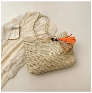 Detail of straw woven tote bag featuring decorative orange tassels and natural texture