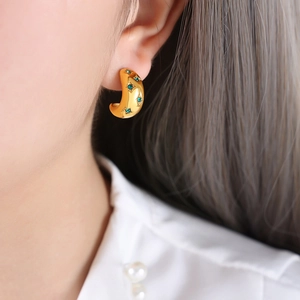 Gros plan d'une boucle d'oreille demi-cercle dorée avec cristaux verts sur un mannequin