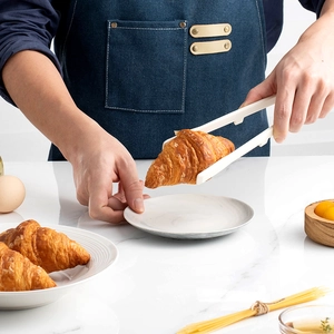Heat-resistant white silicone food tongs for kitchen use holding bread on a bright scene