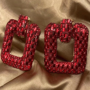 Macro detail of red rhinestone pavé on gold chain earrings over champagne silk fabric