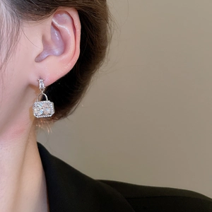 Close-up of square padlock drop earrings with silver plating and cubic zirconia on model