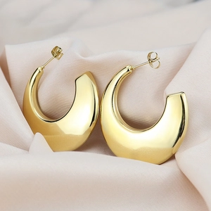 Detailed macro view of gold-plated chunky C-shaped hoop earrings on pink silk
