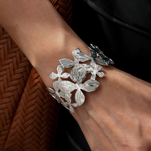 Close-up of wide silver open cuff bracelet featuring intricate hollow floral petal layers