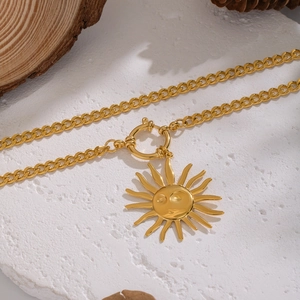 Vintage sun face pendant necklace in gold-tone metal with flat chain on a stone surface