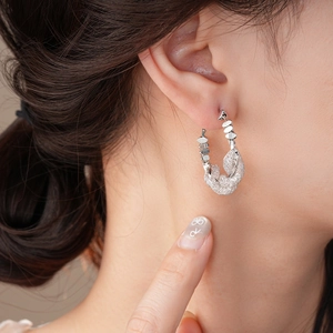 Close-up of minimalist silver intertwined geometric hoop earring worn by a model
